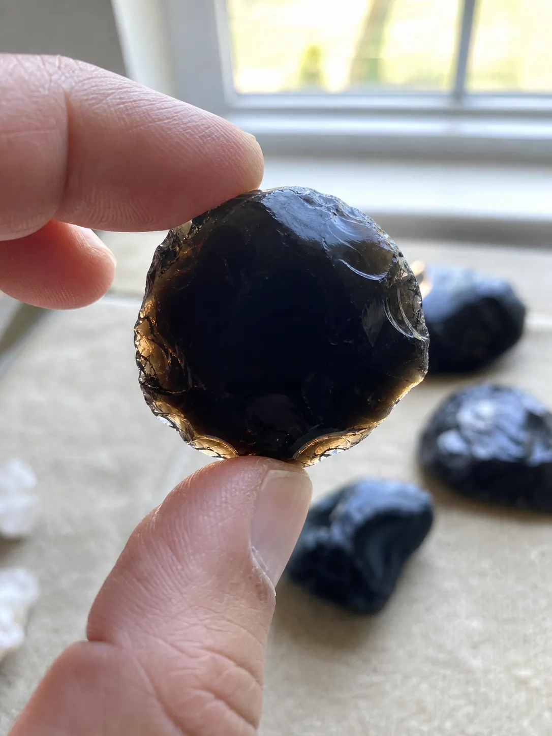Dark obsidian nodule held near bright light showing a smoky translucent edge
