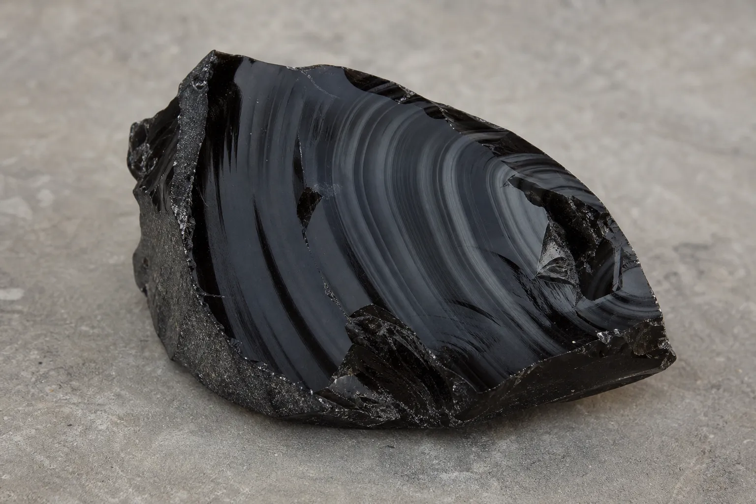 Black obsidian showing subtle gray flow-like bands across a dark polished surface