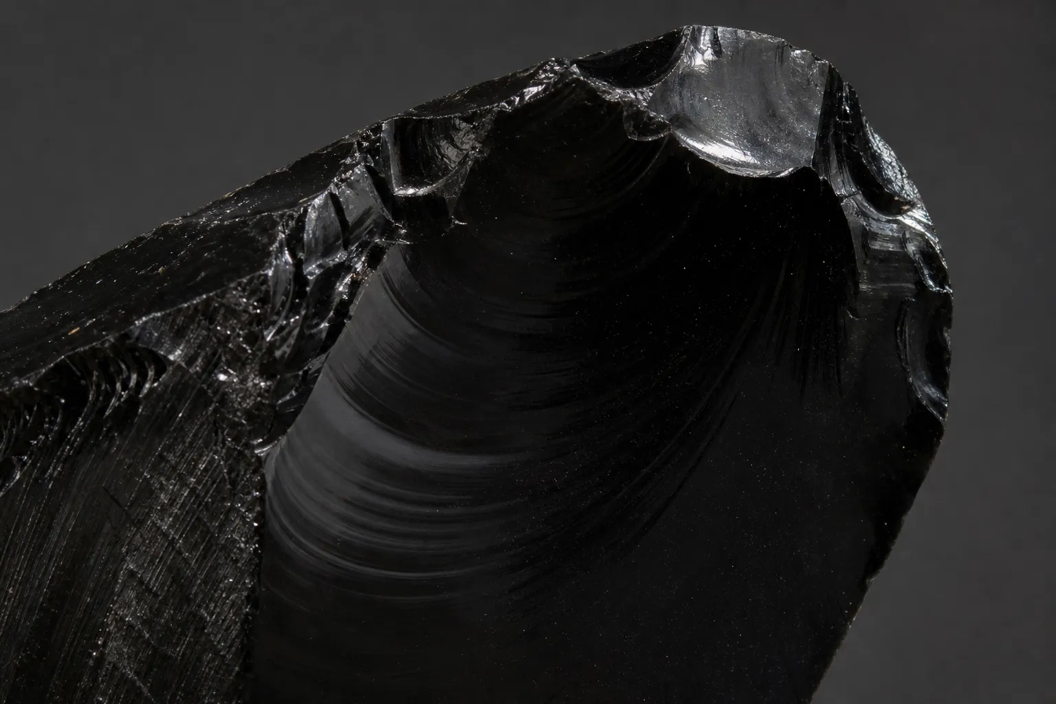 Close view of obsidian with smooth curved fracture and reflective glassy luster