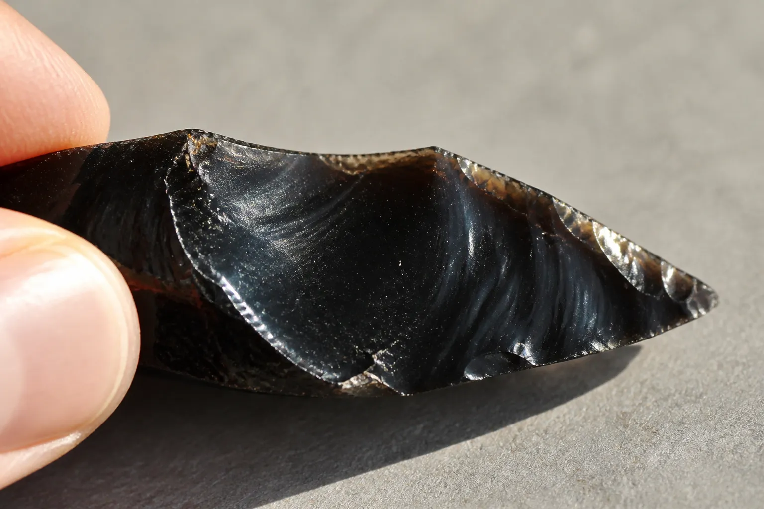 Sharp glassy black stone edge with curved fracture scars used as an obsidian identification clue