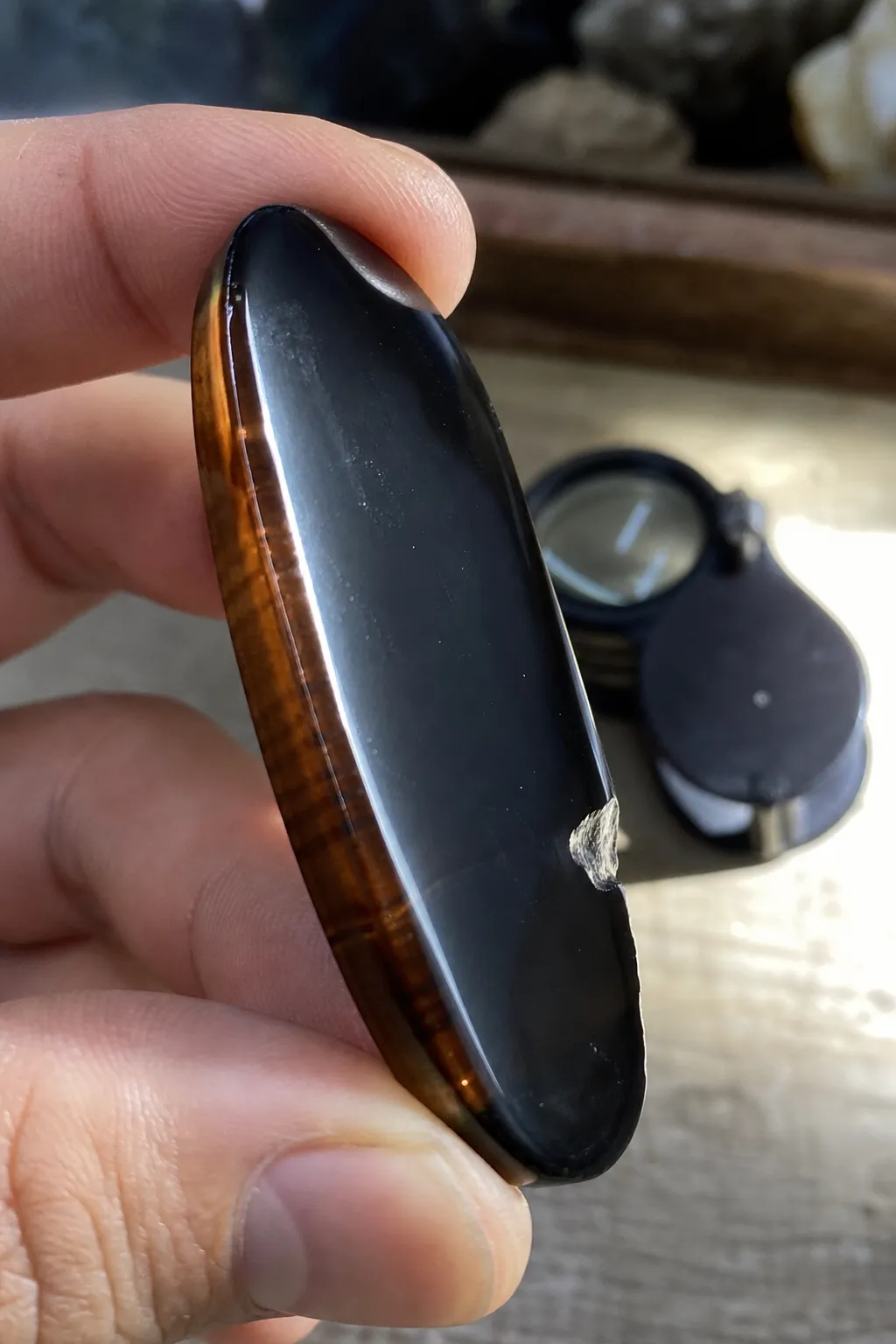 A polished black stone inspected at the edge with side light to reveal possible bands or translucency