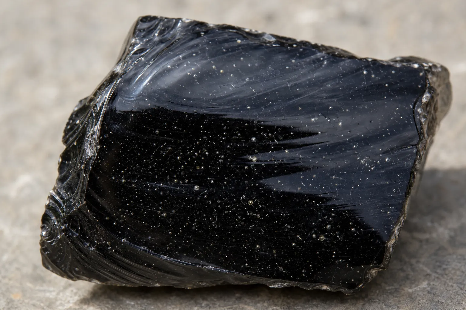 Close view of black obsidian showing tiny internal bubbles and small specks under angled light