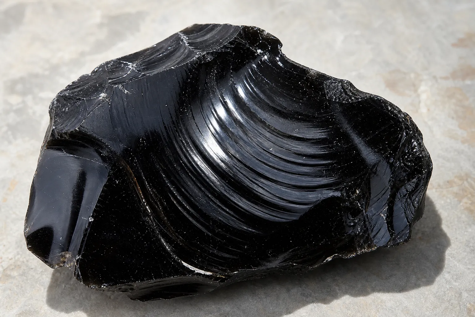 Broken obsidian face showing curved ripple marks on a glossy fracture surface