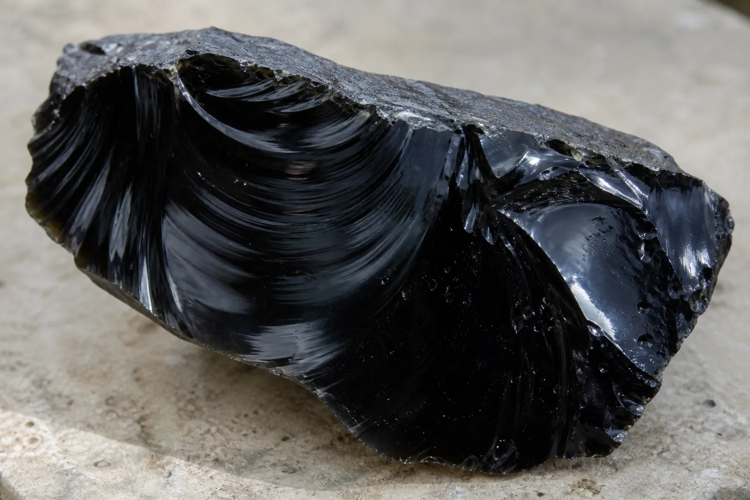 A dark obsidian specimen showing glassy luster and smooth conchoidal fracture surfaces